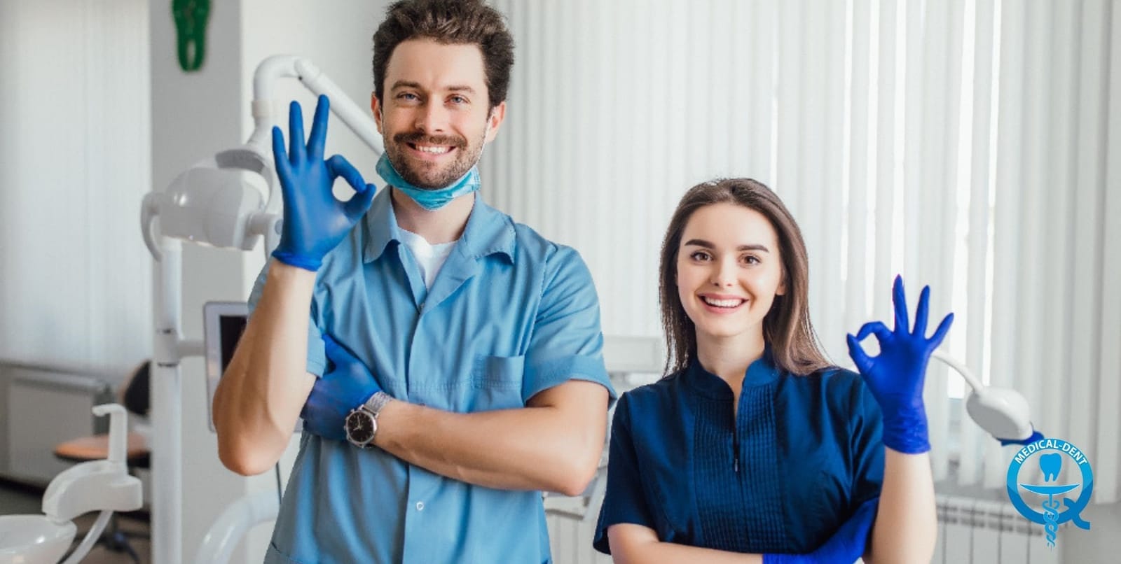 Two people in dental clothing standing beside a treatment chair
