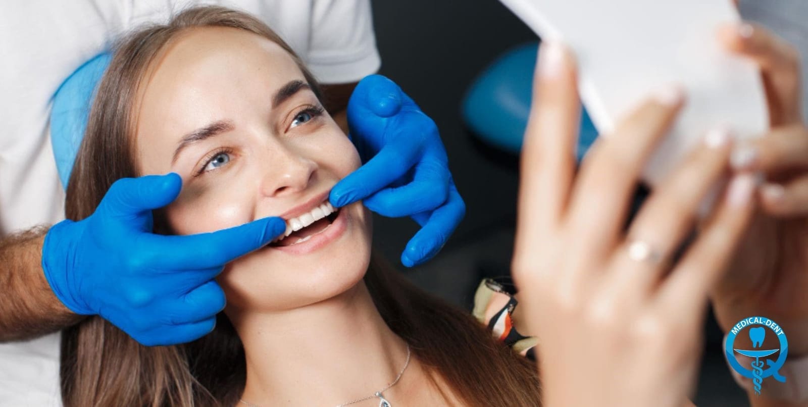 A dentist comparing a patient’s teeth with a shade guide while the patient holds a mirror