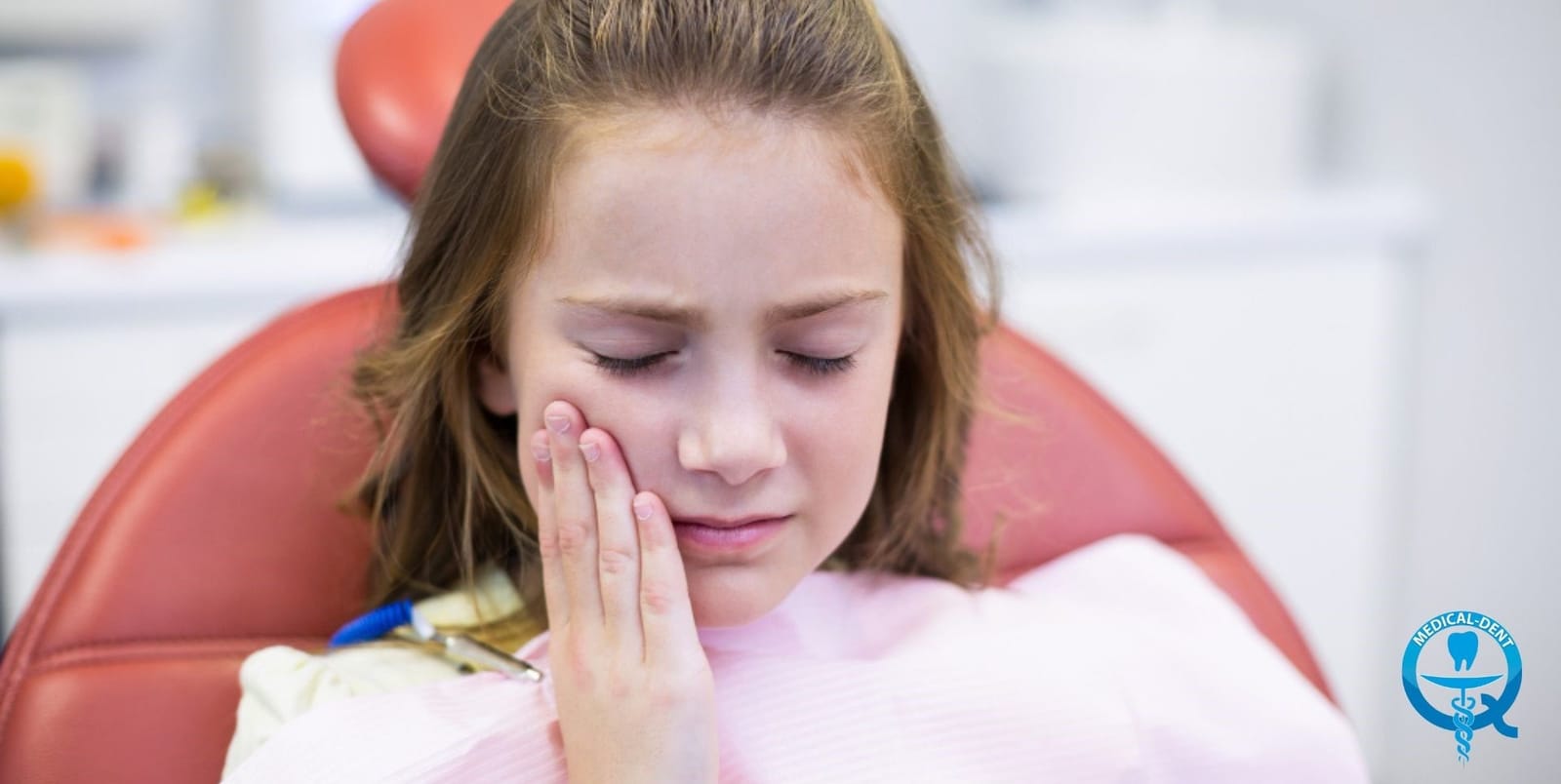 A child holding her cheek while seated in a dental chair