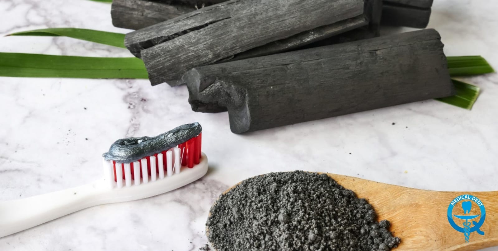 A toothbrush with dark powder beside charcoal and a wooden spoon