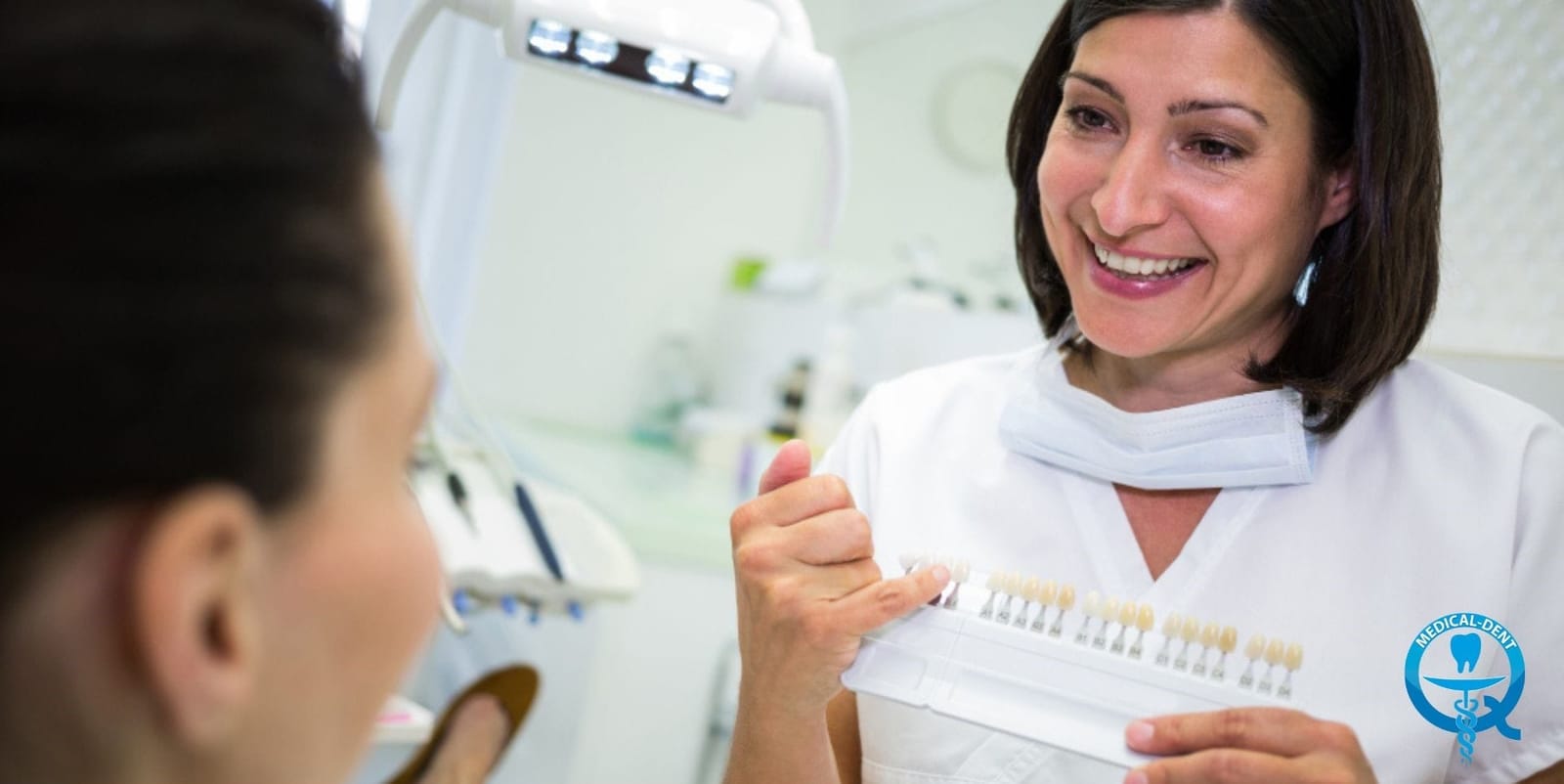 A patient holding a mirror while a clinician shows a tooth shade guide