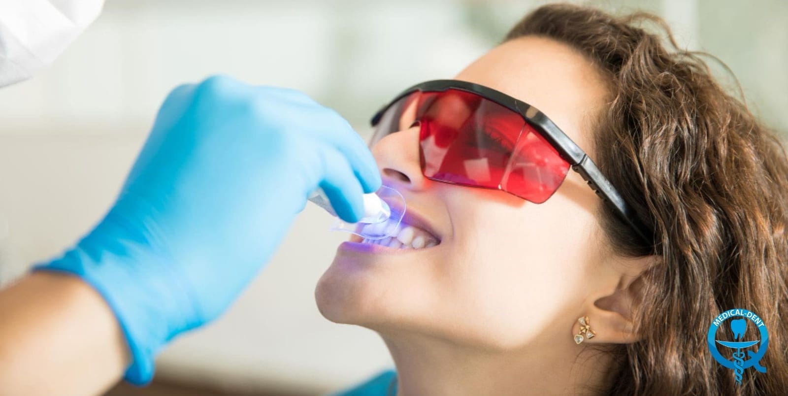 A patient wearing protective glasses with a dental light positioned at the mouth