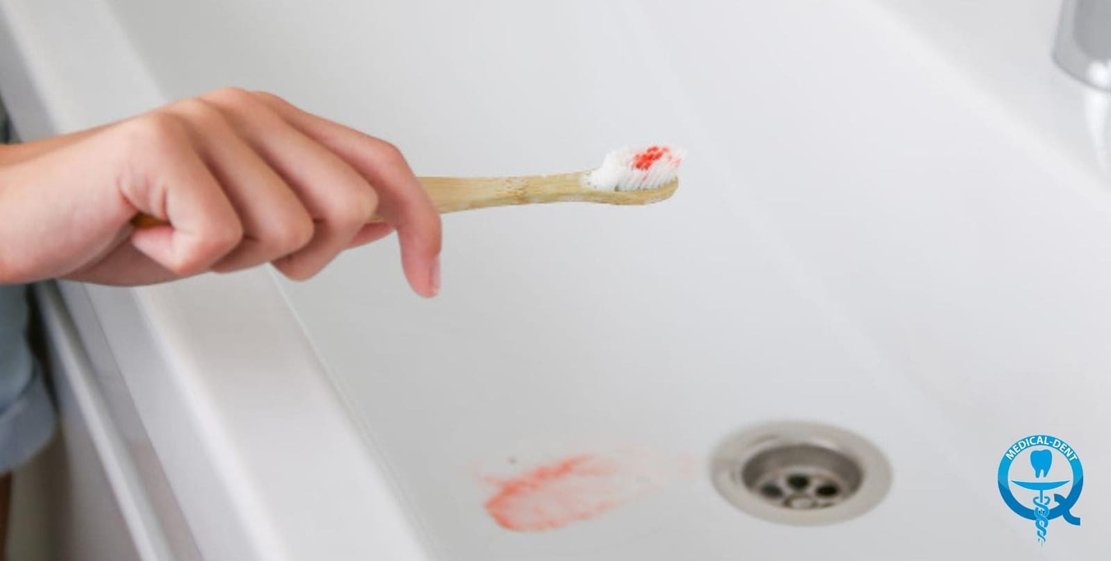 A toothbrush with red-stained toothpaste held over a basin