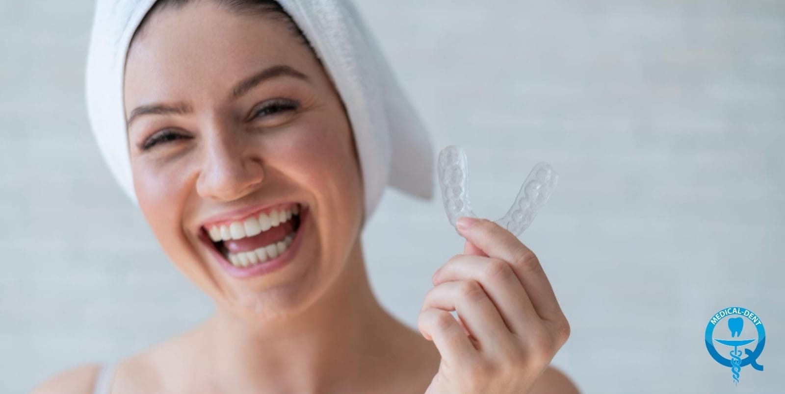 A person with a towel around their head holding a clear dental tray