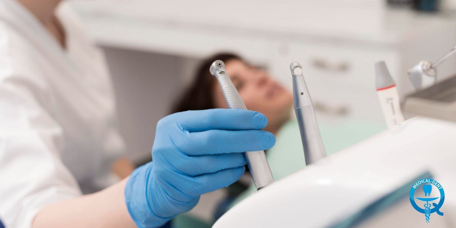 A gloved hand holding a dental handpiece beside a patient